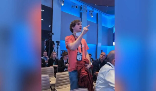 un valiente persona en playera naranja hablando contra el uso de tecnología en el genocidio de Israel en Palestina.